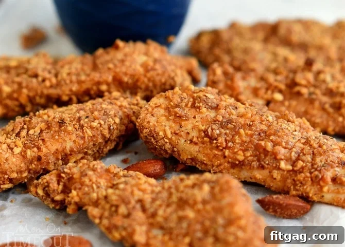 Freshly baked sriracha almond crusted chicken strips on parchment paper, with scattered almond crumbs