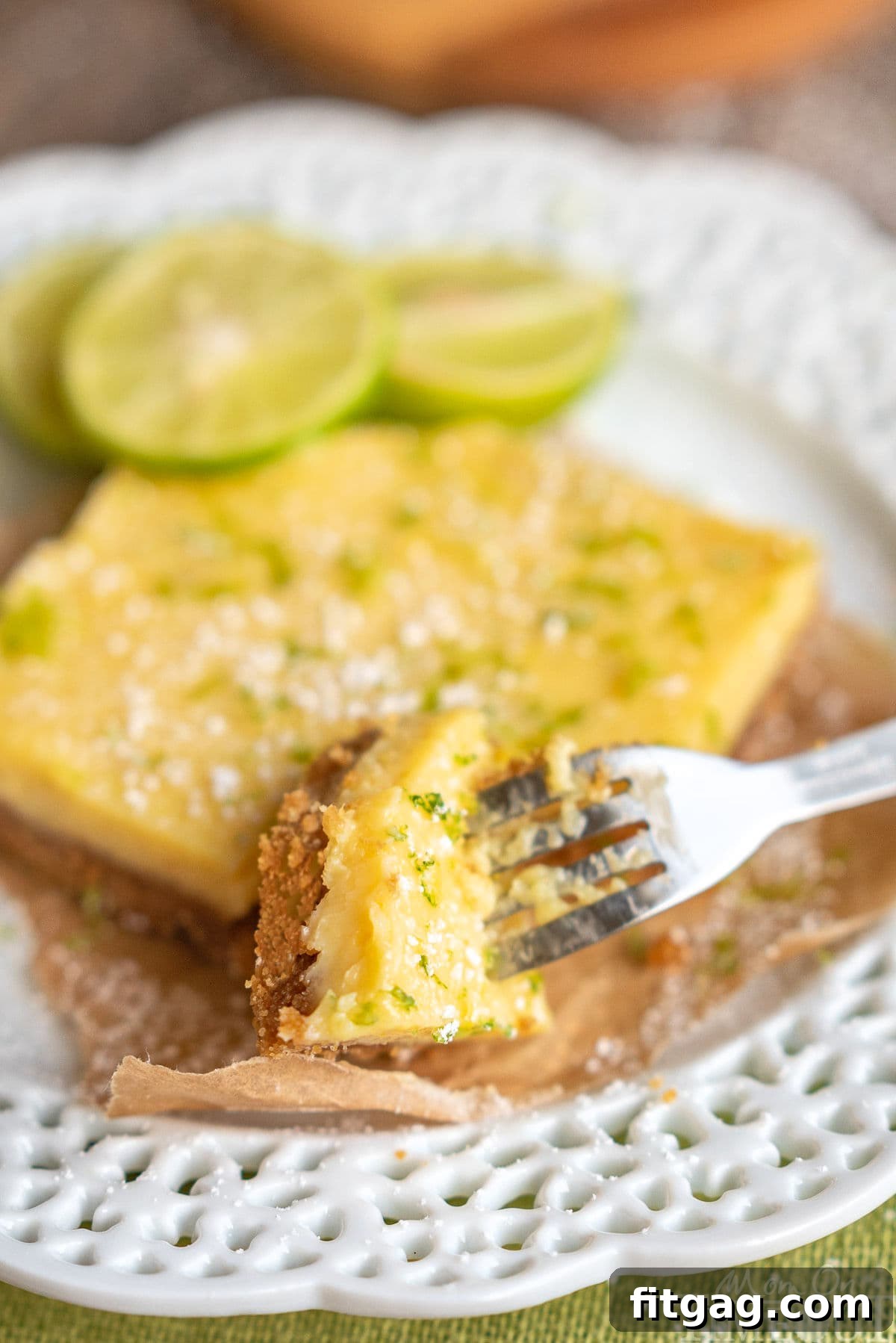 Tangy Key Lime Bars 3 A single Key Lime Pie Bar resting on a pristine white plate, with a corner gently cut away by a fork, revealing its exquisite layers of crust and creamy filling.