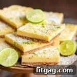 Tangy Key Lime Bars 7 wood cake stand piled high with key lime bars topped with key lime zest and a light dusting of powdered sugar. Slices of lime are scattered around the bars.