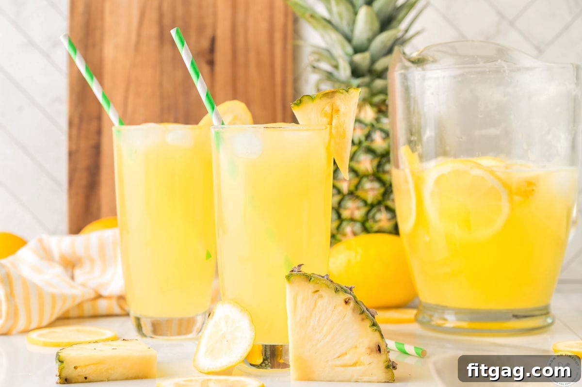 Two glasses filled with pineapple lemonade. Straws in glasses with fresh pineapple in the background.