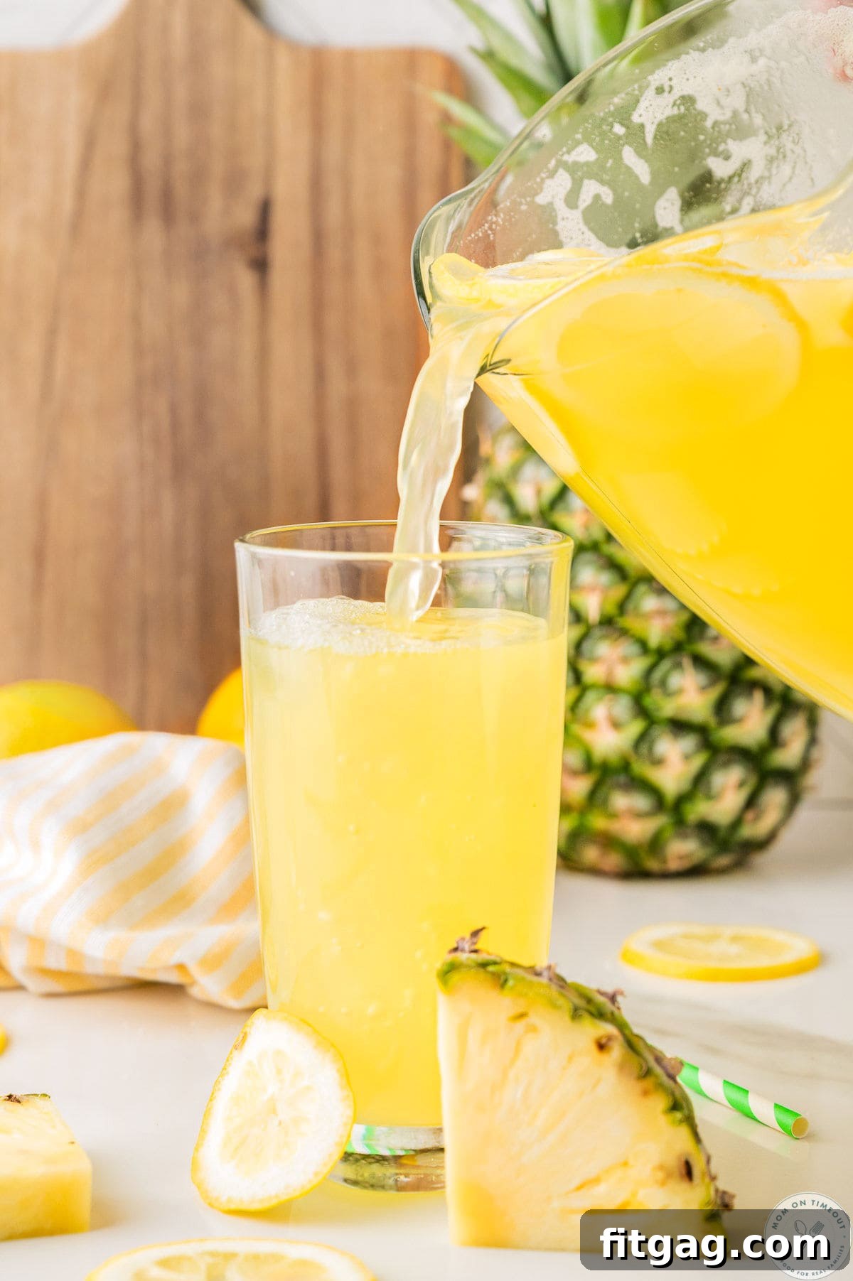Pineapple lemonade drink being poured from a glass pitcher to a glass.