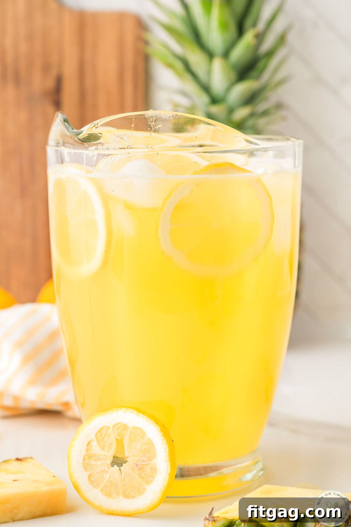 Glass pitcher filled with pineapple lemonade garnished with lemon slices and pineapple wedges.